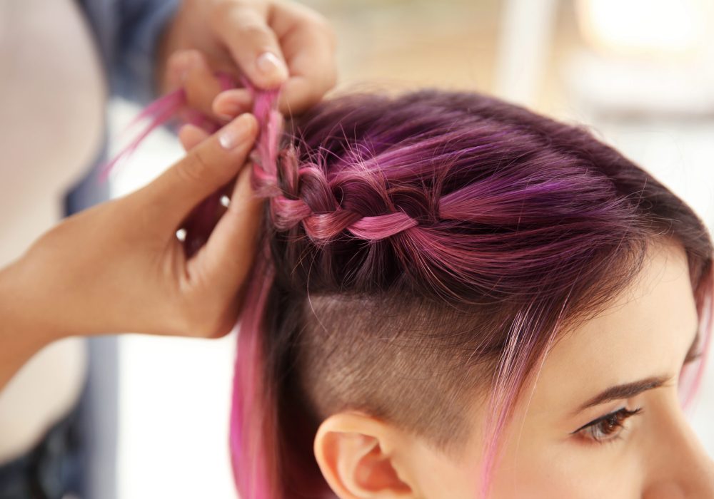 Professional stylist braiding woman's color hair in beauty salon. Modern trend